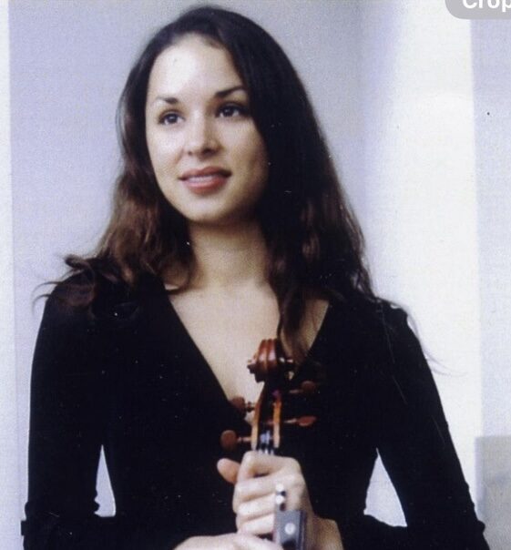 Woman with dark hair wearing a black top, holding a violin in front of her.