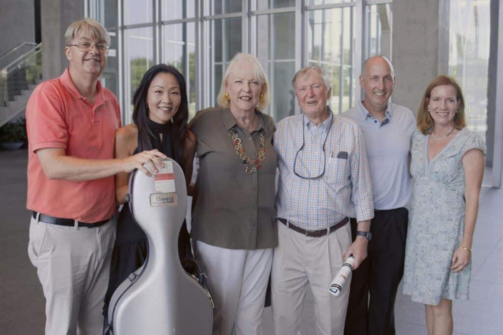 Six adults posing together for a group photo in a bright indoor setting, smiling at the camera.